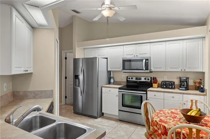 Kitchen with visible vents, appliances with stainless steel finishes, white cabinets, a sink, and vaulted ceiling
