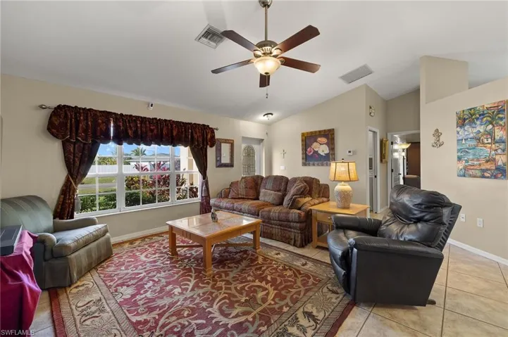 Living area with a ceiling fan, visible vents, vaulted ceiling, and light tile patterned floors