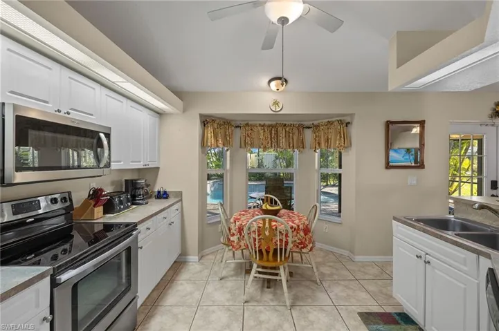 Kitchen with light tile patterned floors, appliances with stainless steel finishes, white cabinetry, a sink, and ceiling fan