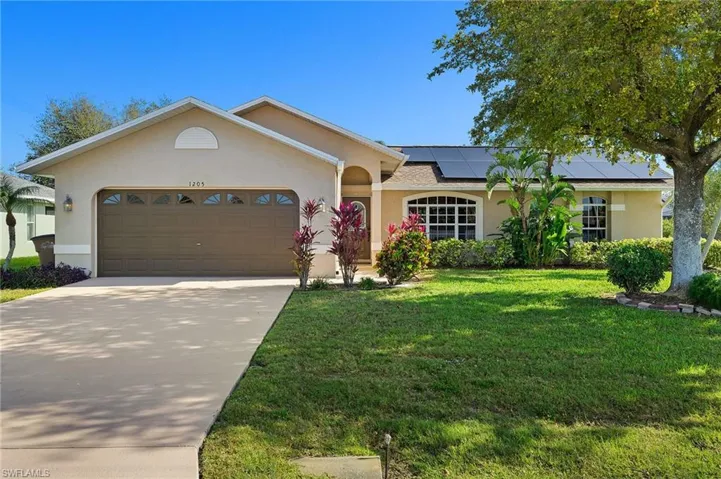 Ranch-style home with a front lawn, roof mounted solar panels, an attached garage, and stucco siding