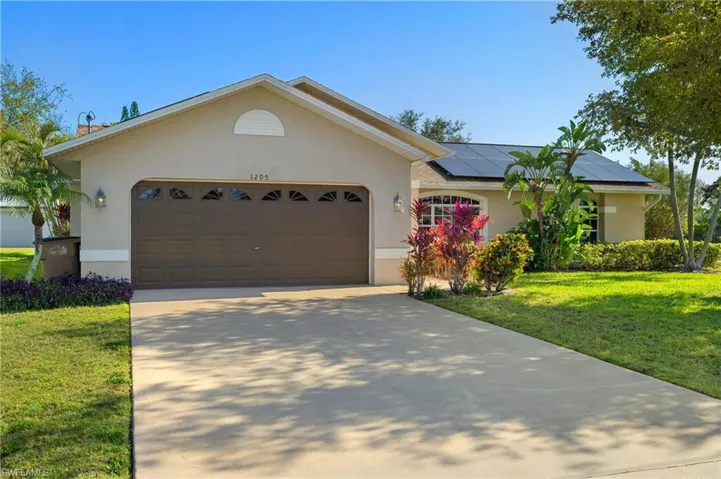 Ranch-style house with a garage, driveway, stucco siding, roof mounted solar panels, and a front yard