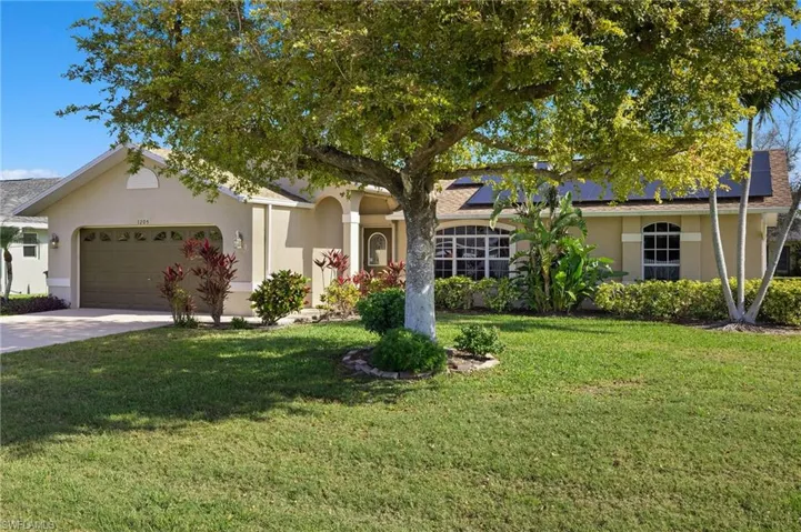 Ranch-style home featuring stucco siding, an attached garage, roof mounted solar panels, driveway, and a front lawn