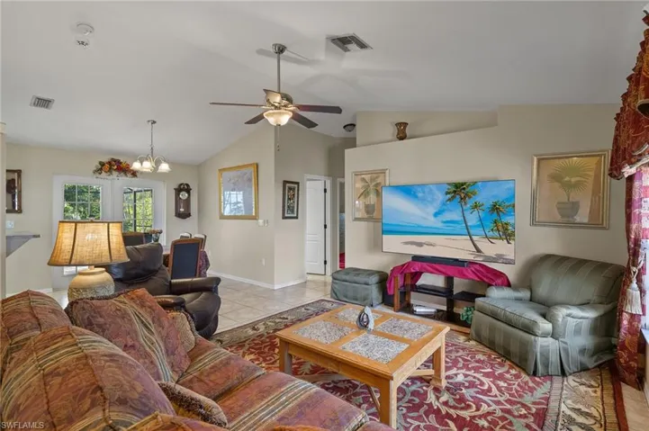 Living room featuring lofted ceiling, light tile patterned floors, visible vents, and ceiling fan with notable chandelier