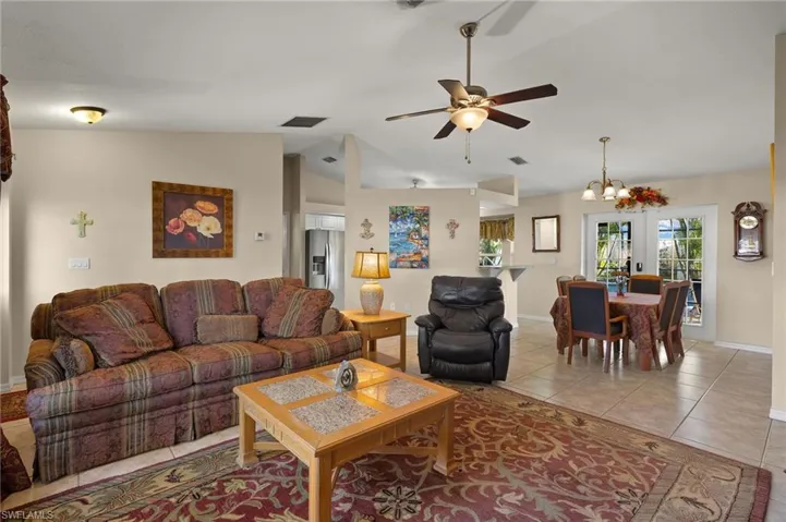 Living room featuring ceiling fan with notable chandelier, visible vents, vaulted ceiling, and light tile patterned flooring