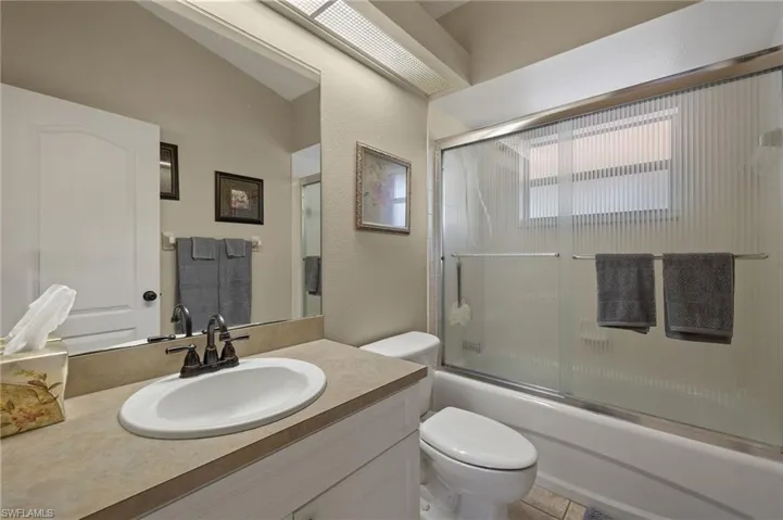 Bathroom with shower / bath combination with glass door, vanity, toilet, and tile patterned floors
