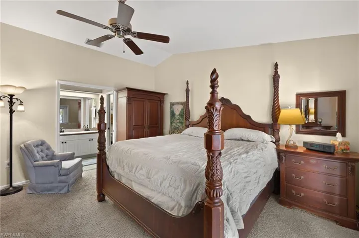 Bedroom featuring carpet, vaulted ceiling, ensuite bath, and ceiling fan