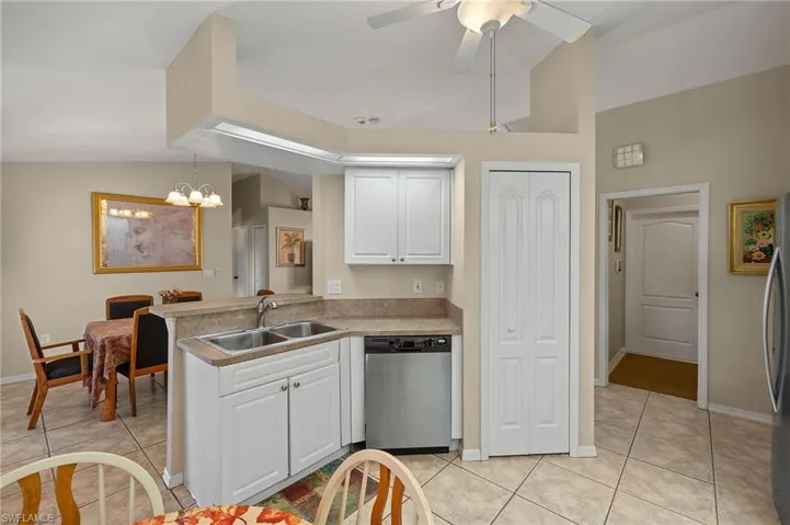 Kitchen featuring stainless steel appliances, white cabinetry, vaulted ceiling, a sink, and light tile patterned flooring