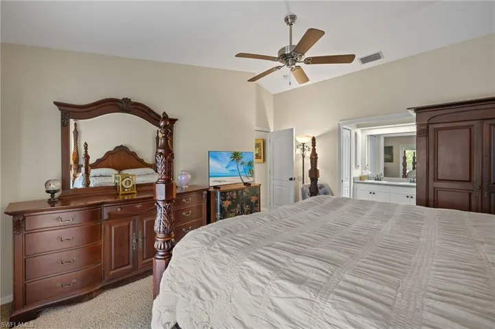 Bedroom featuring lofted ceiling, connected bathroom, light colored carpet, a ceiling fan, and visible vents