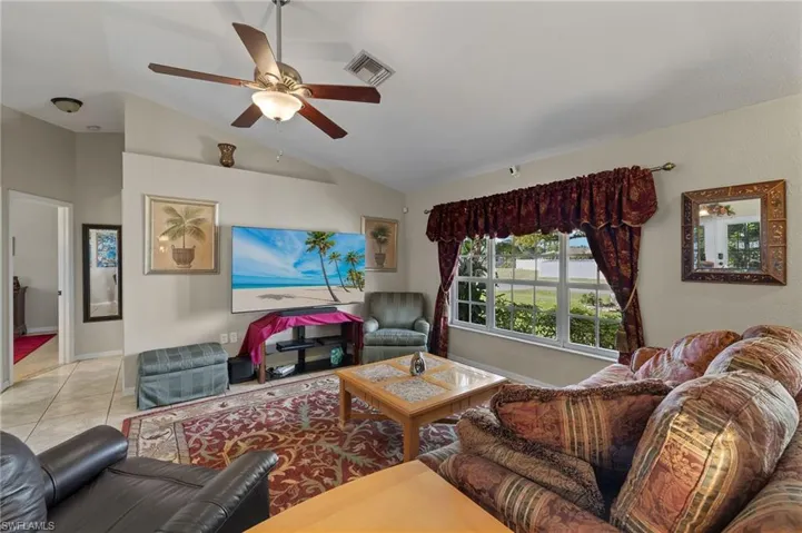 Living area with light tile patterned floors, ceiling fan, vaulted ceiling, and visible vents