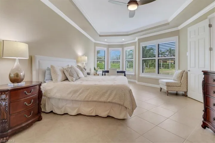Tiled bedroom with a raised ceiling, ceiling fan, and crown molding