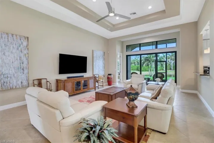 Living room with light tile patterned floors, a towering ceiling, a tray ceiling, and ceiling fan