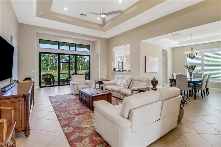 Living room featuring a raised ceiling, light tile patterned flooring, a healthy amount of sunlight, and ceiling fan with notable chandelier