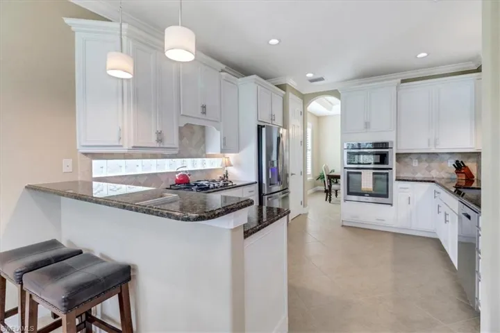 Kitchen featuring white cabinets, a kitchen breakfast bar, hanging light fixtures, kitchen peninsula, and stainless steel appliances