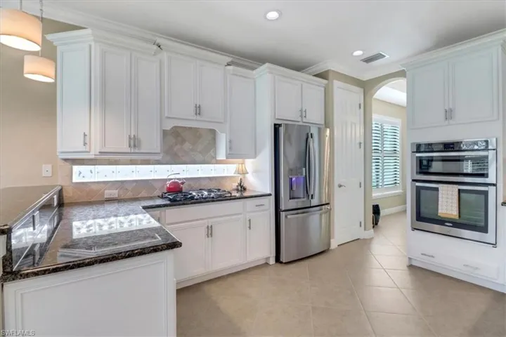 Kitchen with backsplash, white cabinetry, hanging light fixtures, and appliances with stainless steel finishes