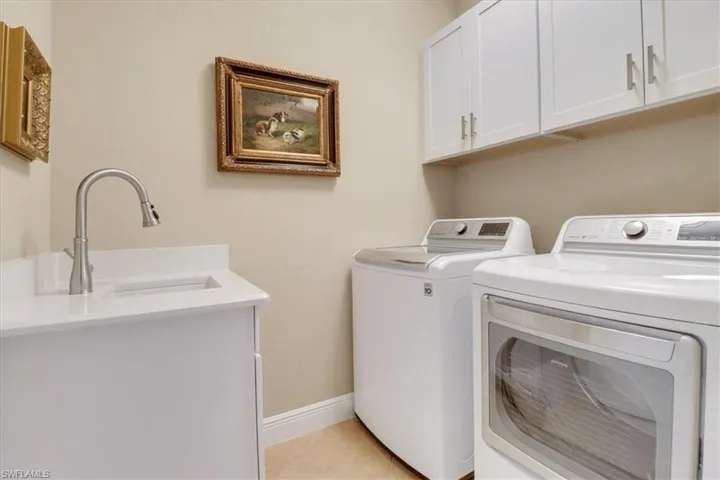 Laundry area featuring cabinets, light tile patterned floors, washing machine and dryer, and sink