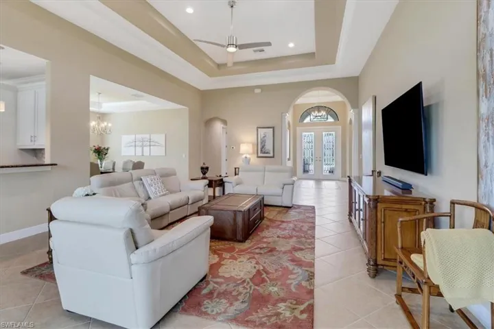 Living room featuring ceiling fan with notable chandelier, a raised ceiling, and light tile patterned floors