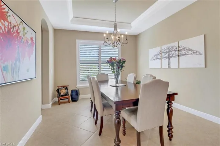 Dining area with a tray ceiling, light tile patterned flooring, a chandelier, and ornamental molding