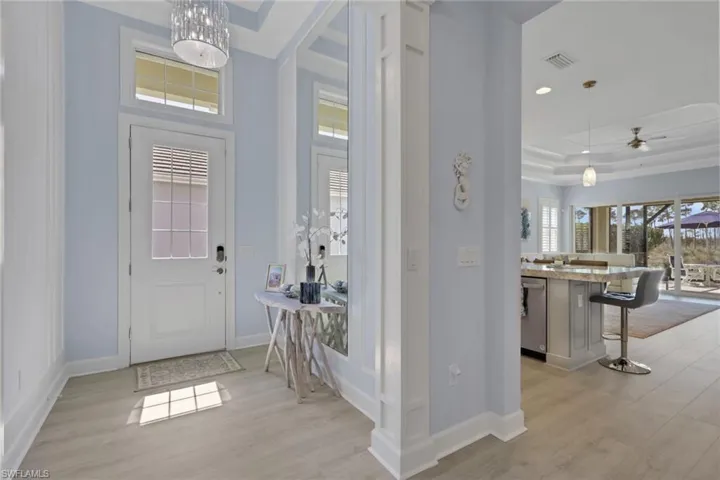 Foyer entrance with light wood-style floors, a raised ceiling, ceiling fan, and suspended lighting