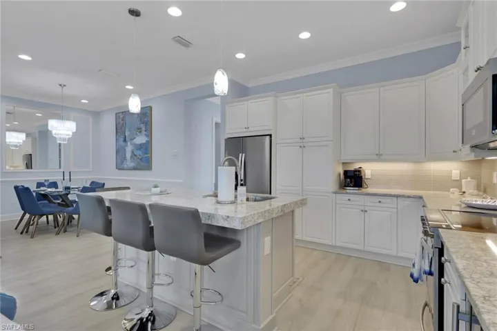 Kitchen featuring ornamental molding, white cabinetry, a kitchen island with sink, decorative light fixtures, and light wood-style floors