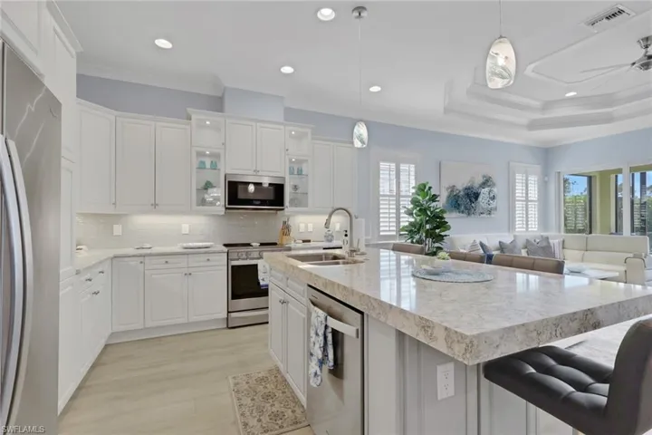 Kitchen featuring stainless steel appliances, hanging light fixtures, white cabinetry, light stone countertops, and open floor plan