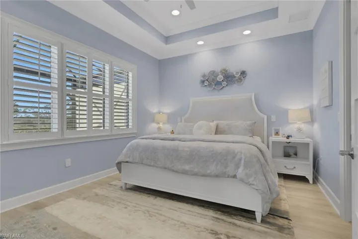 Bedroom featuring wood finished floors, a ceiling fan, recessed lighting, a tray ceiling, and crown molding
