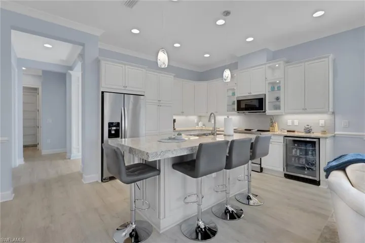 Kitchen with white cabinetry, a breakfast bar, wine cooler, stainless steel appliances, and hanging light fixtures