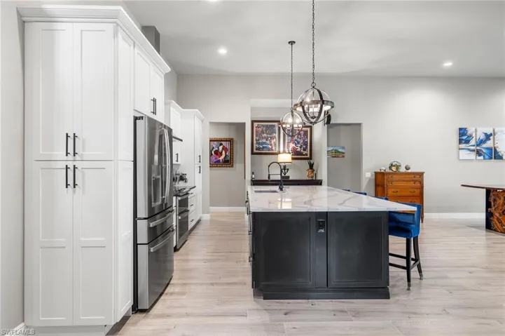 Kitchen featuring a kitchen breakfast bar, appliances with stainless steel finishes, dark cabinetry, light stone countertops, and a center island with sink