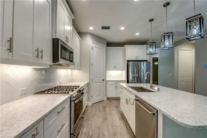 Modern kitchen featuring white shaker cabinetry, stainless steel appliances, light-toned countertops, a herringbone tile backsplash, and wood-finish flooring