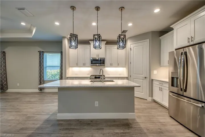 Contemporary kitchen featuring an island with a double sink, stainless steel appliances, white cabinetry with under-cabinet lighting, and wood-finish flooring