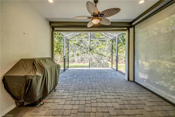 Expansive screened patio featuring paver flooring, a ceiling fan with integrated lighting, and integrated privacy screens