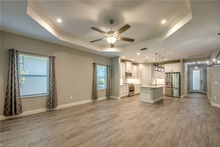 Open-concept living area featuring wood-finish tile flooring, a tray ceiling with recessed lighting, and a ceiling fan
