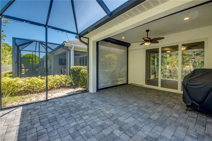 Expansive screened patio featuring paver flooring, a ceiling fan with integrated lighting, and integrated privacy screens