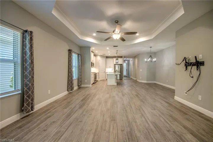 Open-concept living space featuring wood-finish flooring, a tray ceiling, and a ceiling fan with integrated lighting