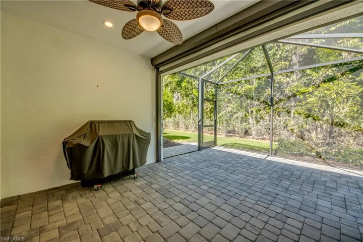 Expansive screened patio featuring paver flooring, a ceiling fan with integrated lighting, and integrated privacy screens