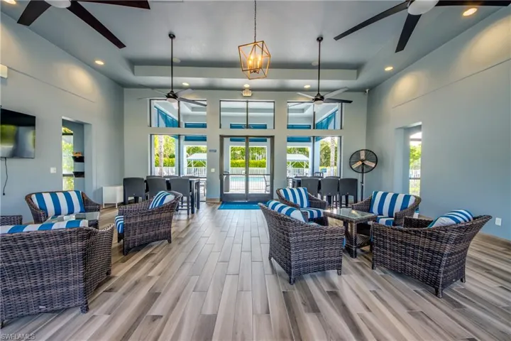 Spacious lounge area featuring wood-finish flooring, a tray ceiling with recessed lighting, and multiple ceiling fans