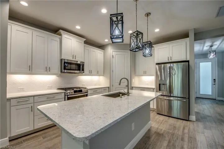 Modern kitchen featuring a large center island with an undermount sink, stainless steel appliances, white shaker cabinetry, white herringbone tile backsplash, and recessed lighting