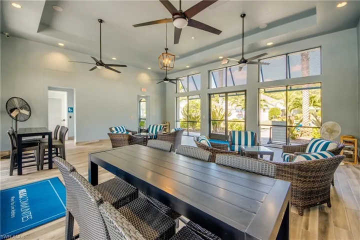 Spacious communal area featuring light wood-finish flooring, a tray ceiling with recessed lighting, and multiple ceiling fans