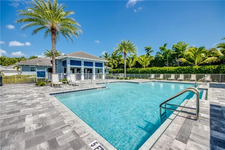 Expansive outdoor community pool area featuring a rectangular pool with integrated steps, surrounding paver patio, and metal perimeter fencing