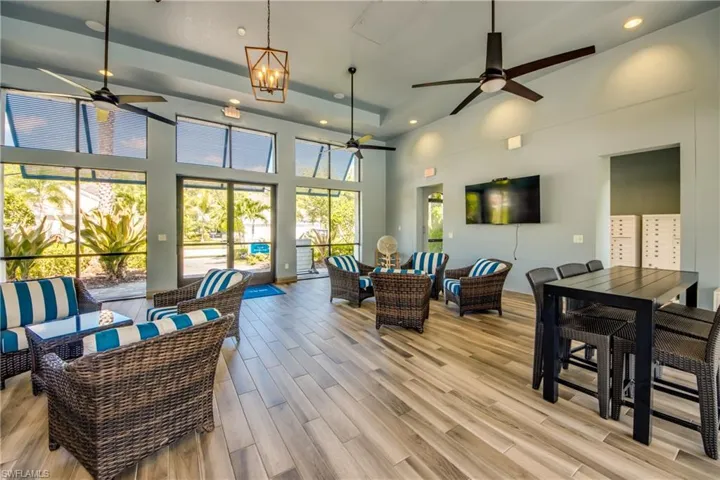 Spacious lounge area featuring wood-finish flooring, a tray ceiling with recessed lighting, and multiple ceiling fans