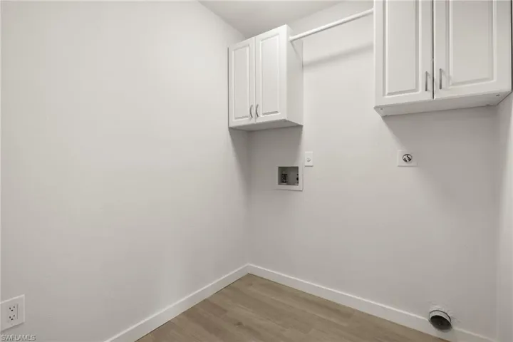 Clothes washing area with cabinets, light hardwood / wood-style floors, electric dryer hookup, and hookup for a washing machine