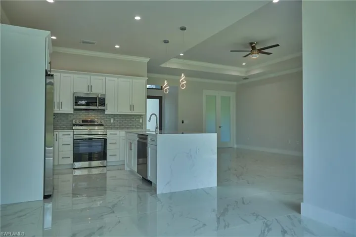 Kitchen featuring ceiling fan, light tile floors, hanging light fixtures, white cabinetry, and appliances with stainless steel finishes