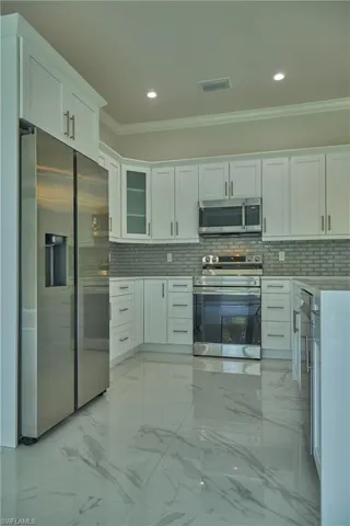 Kitchen with light tile flooring, stainless steel appliances, crown molding, and backsplash