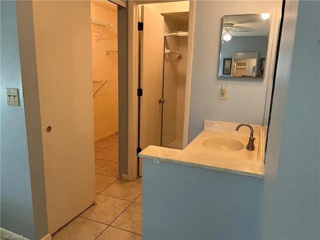 Full bathroom with tile patterned floors, a ceiling fan, a shower, vanity, and a walk in closet