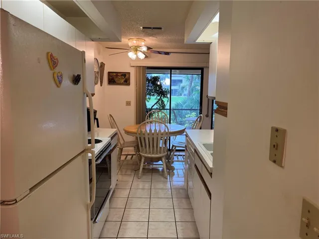 Kitchen with freestanding refrigerator, a ceiling fan, light tile patterned flooring, white cabinets, and range with electric cooktop