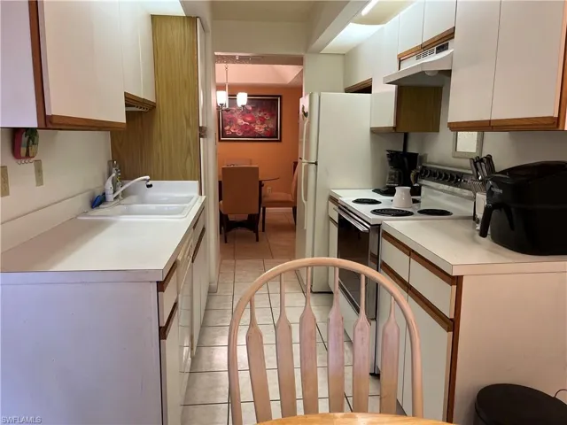 Kitchen with white appliances, white cabinets, under cabinet range hood, light countertops, and light tile patterned floors