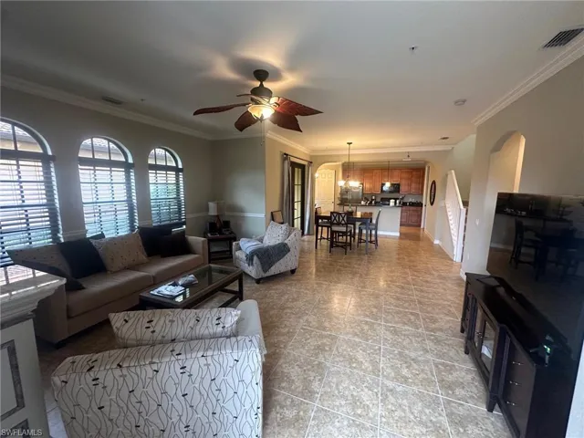 Living room featuring ceiling fan, crown molding, arched walkways, and light tile patterned floors