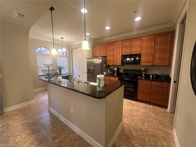 Kitchen with brown cabinetry, black appliances, crown molding, decorative light fixtures, and dark stone counters