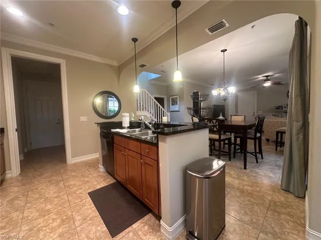 Kitchen featuring decorative light fixtures, dark stone countertops, brown cabinets, dishwasher, and crown molding