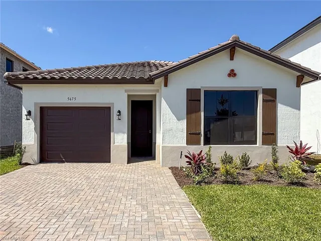 View of front facade featuring a tile roof, decorative driveway, a garage, and stucco siding