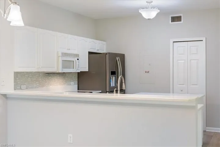 Kitchen featuring stainless steel fridge, white microwave, white cabinetry, and light countertops